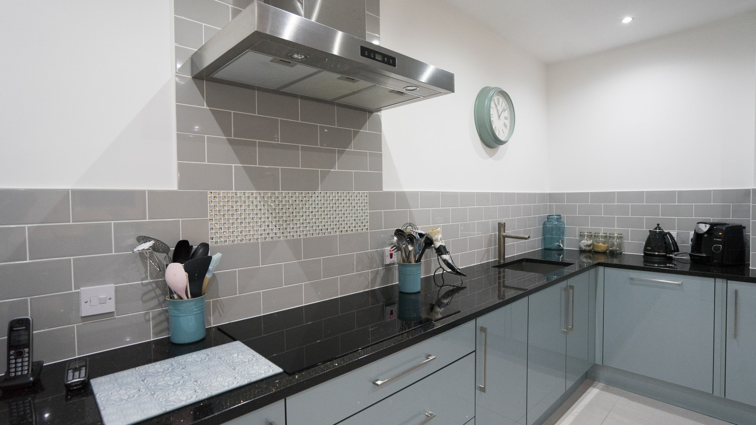 Blue gloss kitchen  with grey tiled splash back, large mirror finish black cooking hob and under-mount sink.