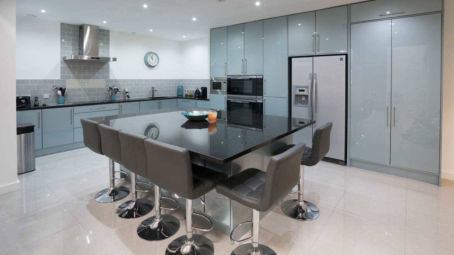 A large granite topped island with overhang and bar stools take center stage of this large high gloss kitchen.
