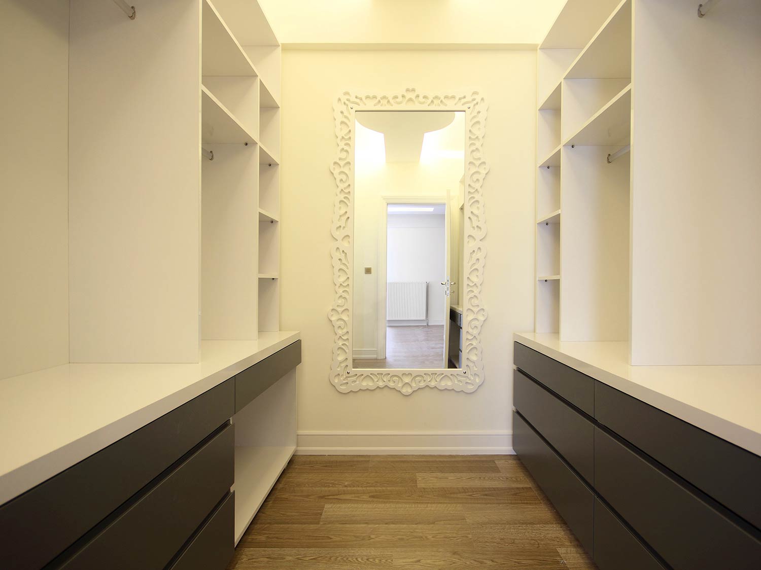 Contemporary walk in wardrobe with anthracite grey draw units and white shelving. This solution has been designed specifically for a client and features a space for a mirror to be used when getting ready.