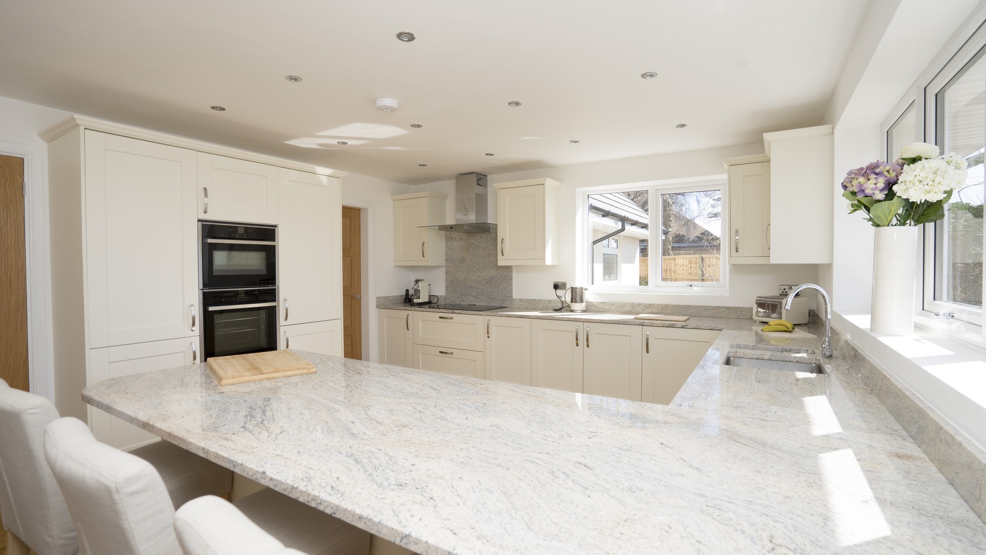 Large Ivory shaker kitchen with stainless steel handles and granite worktops. The granite has been cantilevered over the kitchen cupboards to create an island style dining area.